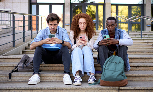 Three students siting on steps scrolling through cell phones