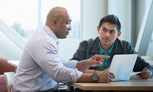 Two woman in grass with book and laptop